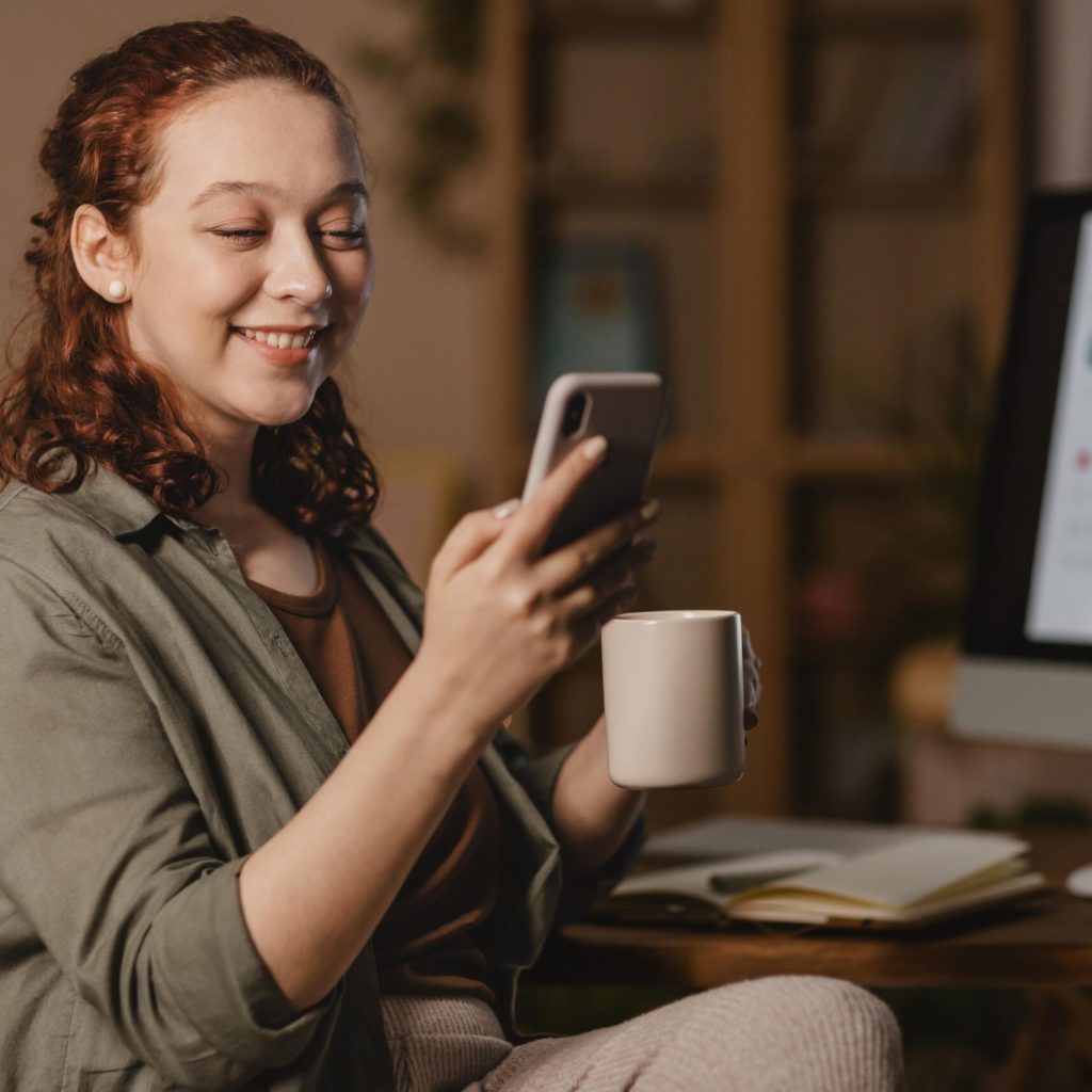 mulher-em-casa-usando-smartphone-na-frente-do-computador-enquanto-toma-cafe